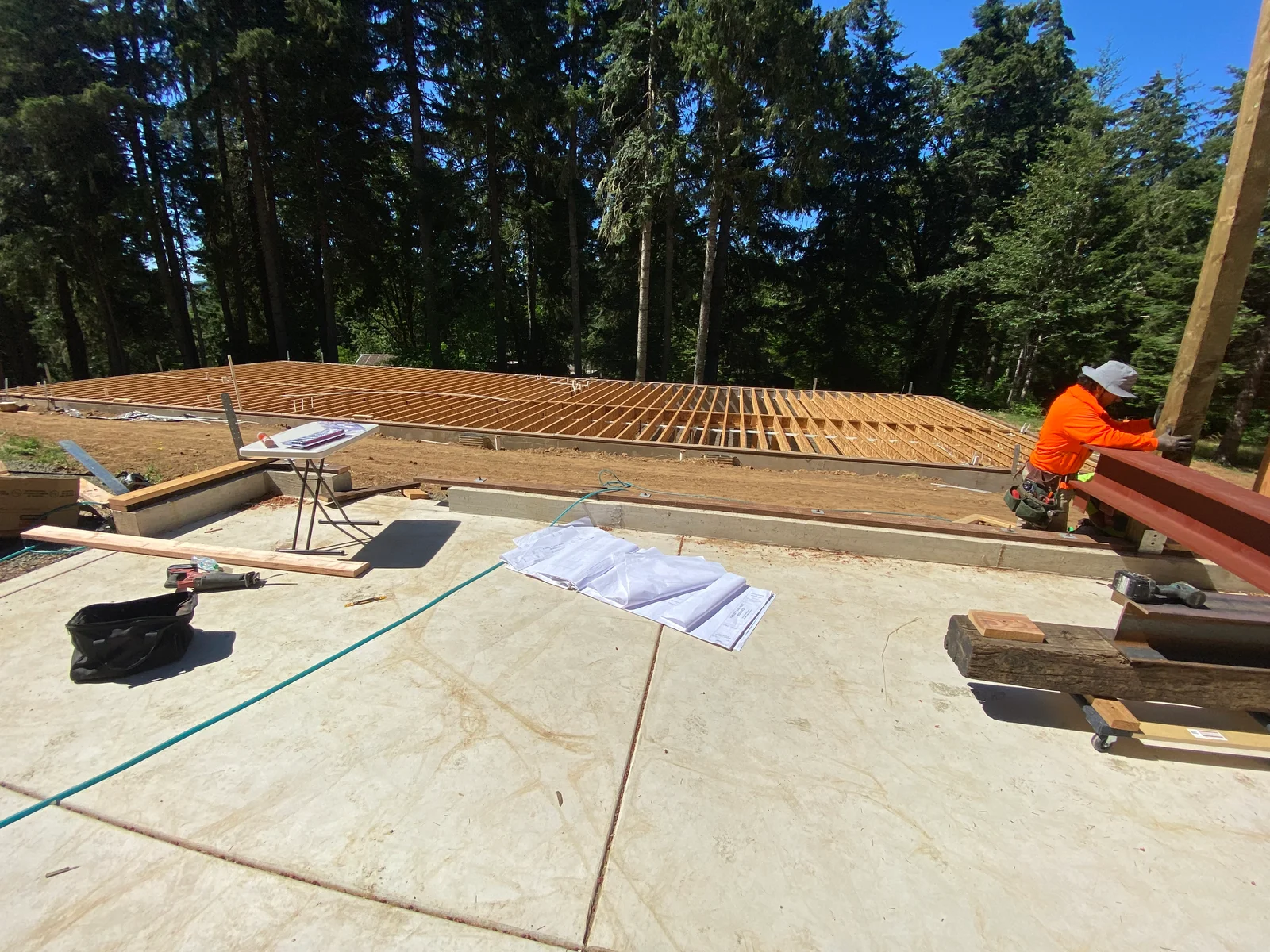 Wood floor framing with joists on concrete foundation, steel support beams, forest backdrop