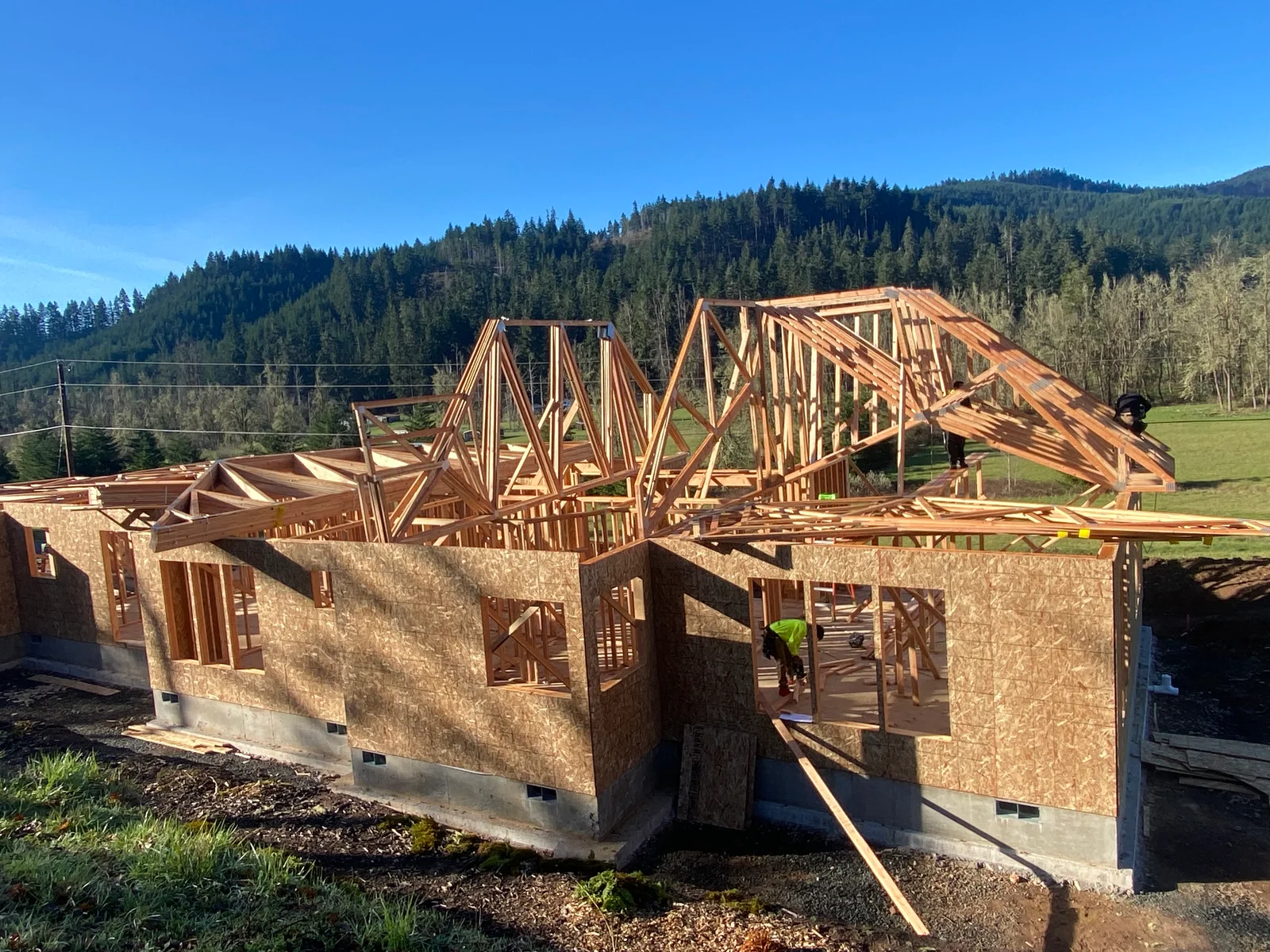 Wood-framed residential structure with OSB sheathing, concrete foundation, and exposed roof trusses during construction