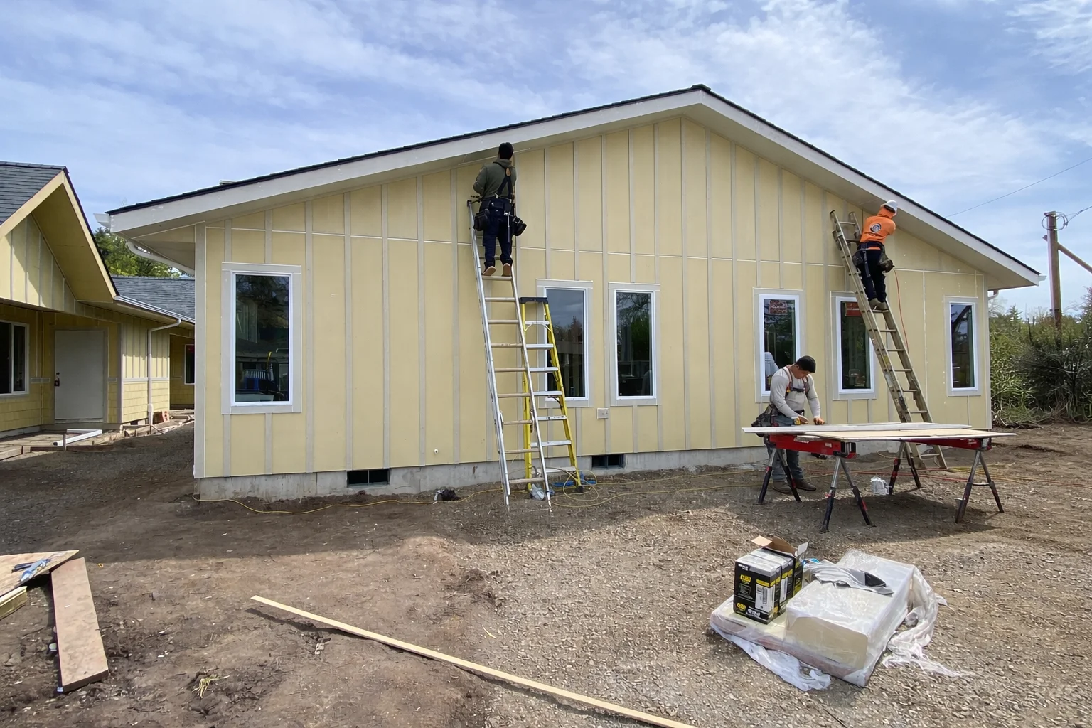 Cream vertical board and batten siding installation with white trim windows on residential addition