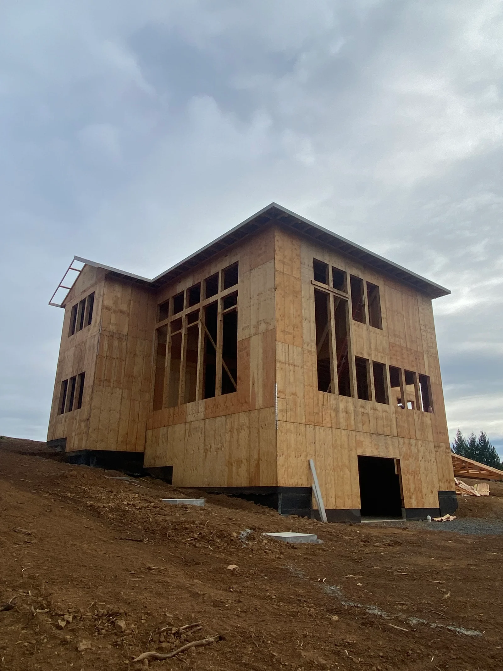 Two-story house frame with OSB sheathing, multiple windows, and elevated foundation on dirt lot