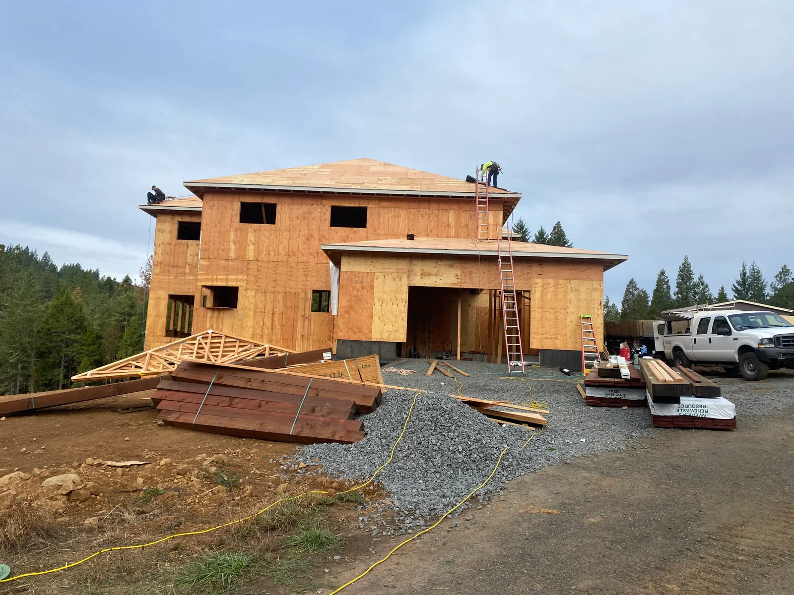 Two-story home framing with plywood sheathing, open windows, and roof trusses under construction
