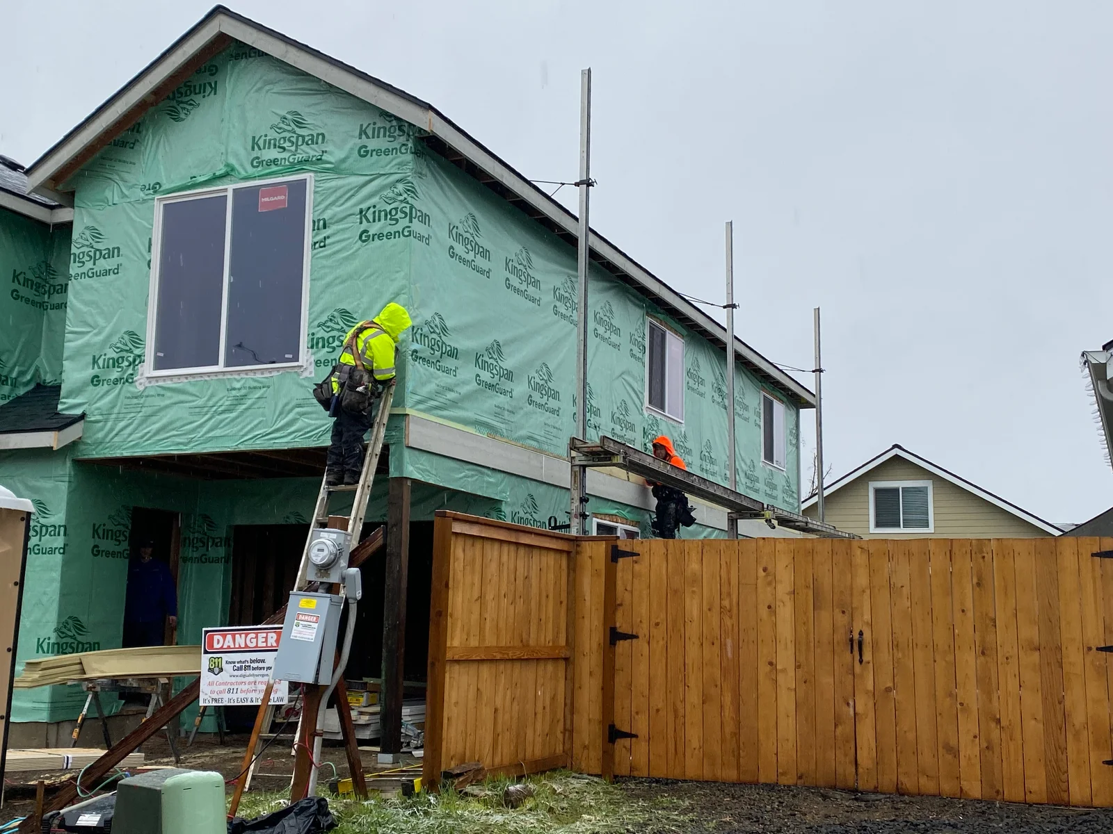 House wrapped in green Kingspan GreenGuard barrier with new windows and worker on ladder