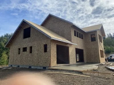Two-story home with stone veneer siding, gable roof sections, and multiple window openings during construction phase