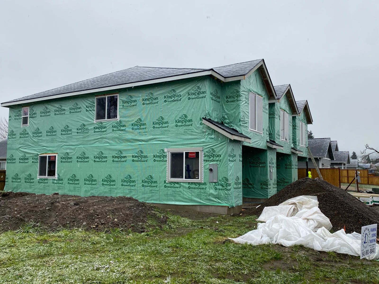 Two-story home wrapped in green Kingspan GreenGuard weather barrier during siding installation
