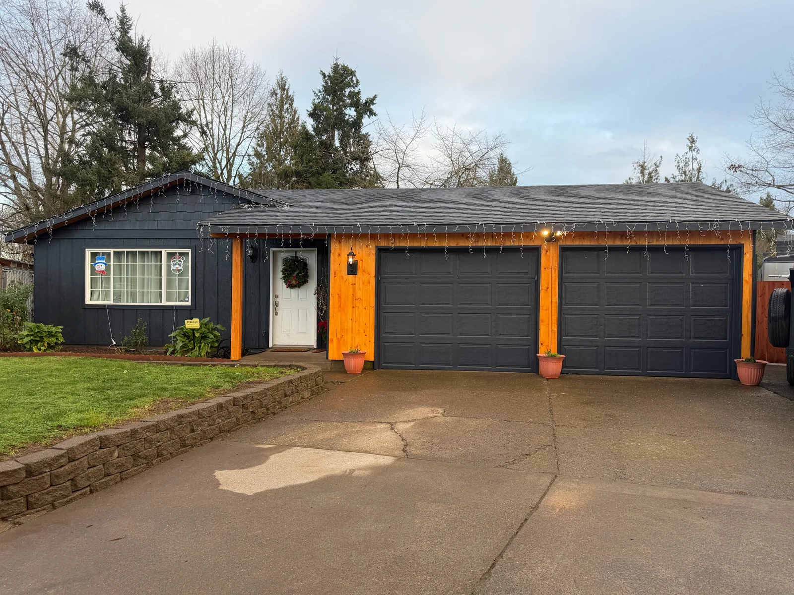 Dark siding with orange trim, black garage doors, new roof, and brick retaining wall