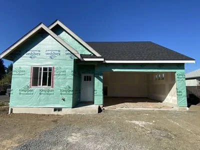 New home with turquoise house wrap, gabled roof, and garage opening during construction phase