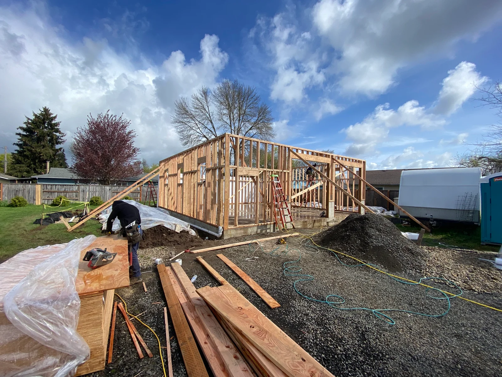 Wooden framing structure with roof trusses, concrete foundation, and gravel base during construction phase