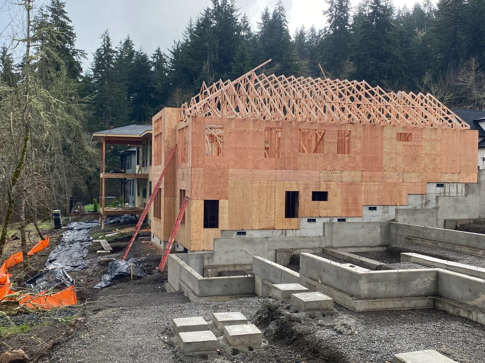 Residential home framing with roof trusses, OSB sheathing, and concrete foundation work in progress