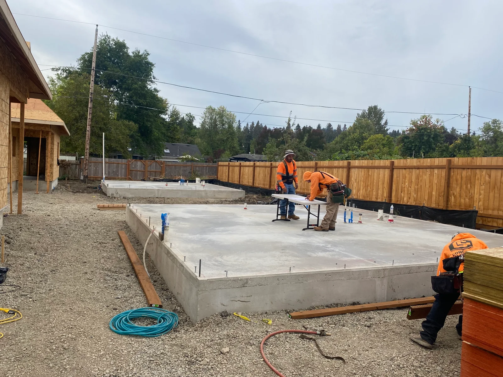 Concrete foundation slab with control joints, wood fence, and construction crew in safety gear