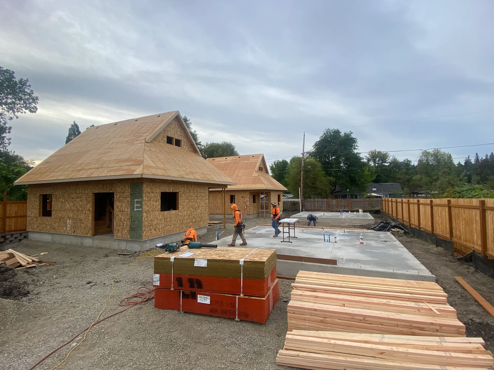 Wood shingle siding on new home construction with pitched roof and concrete foundation work in progress