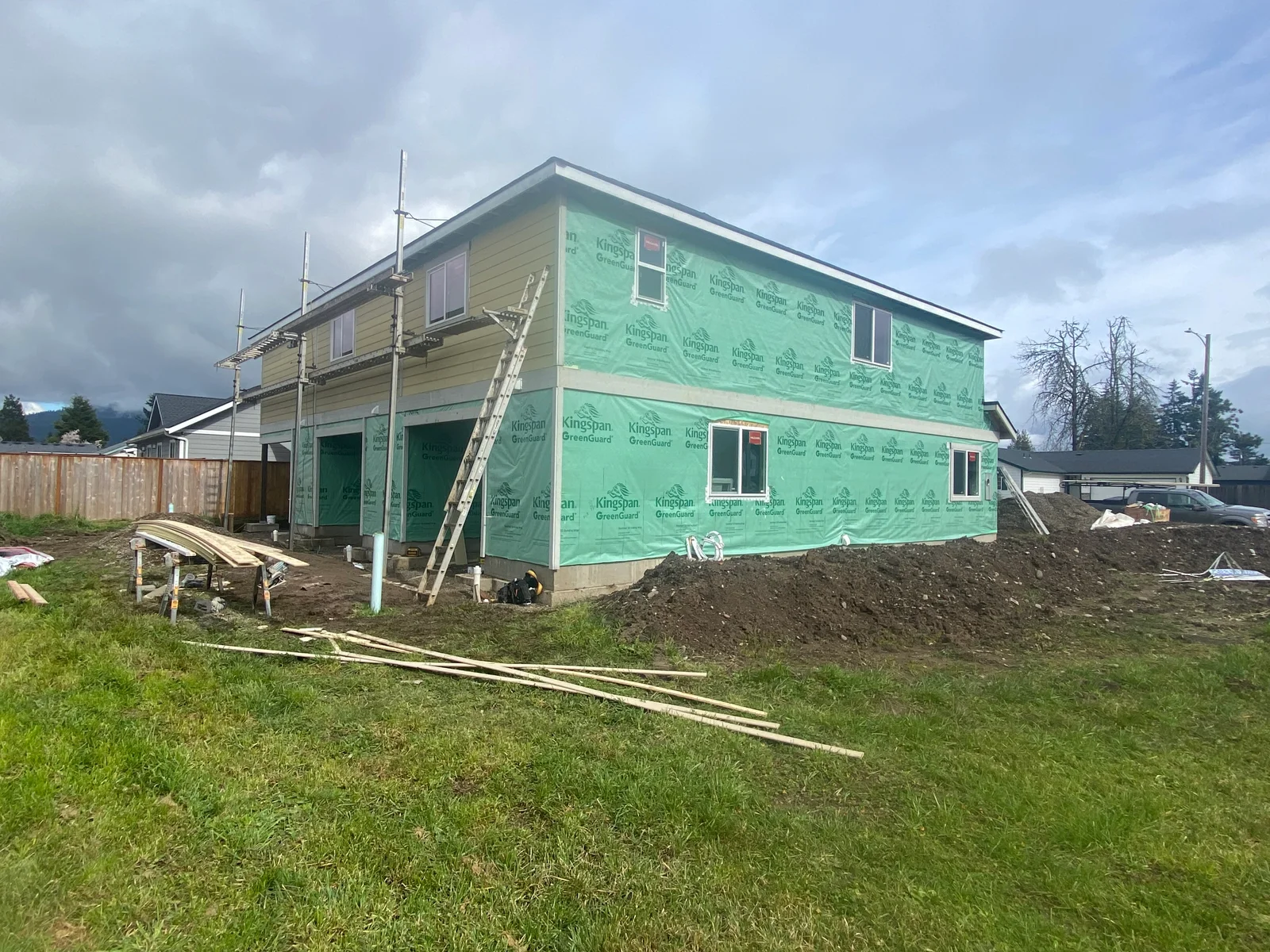 Two-story house with green Kingspan GreenGuard weather barrier and vinyl siding installation in progress