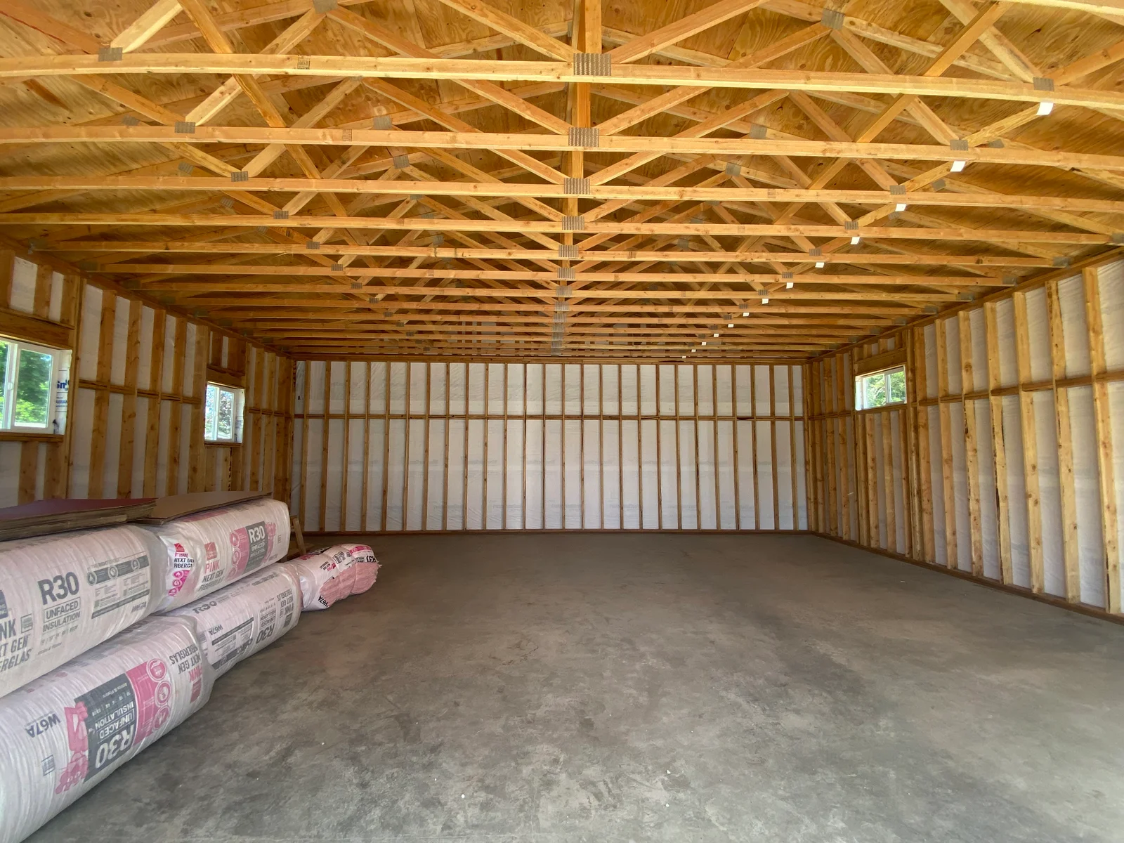 Interior framing with engineered trusses, studs, and R30 insulation batts staged for installation