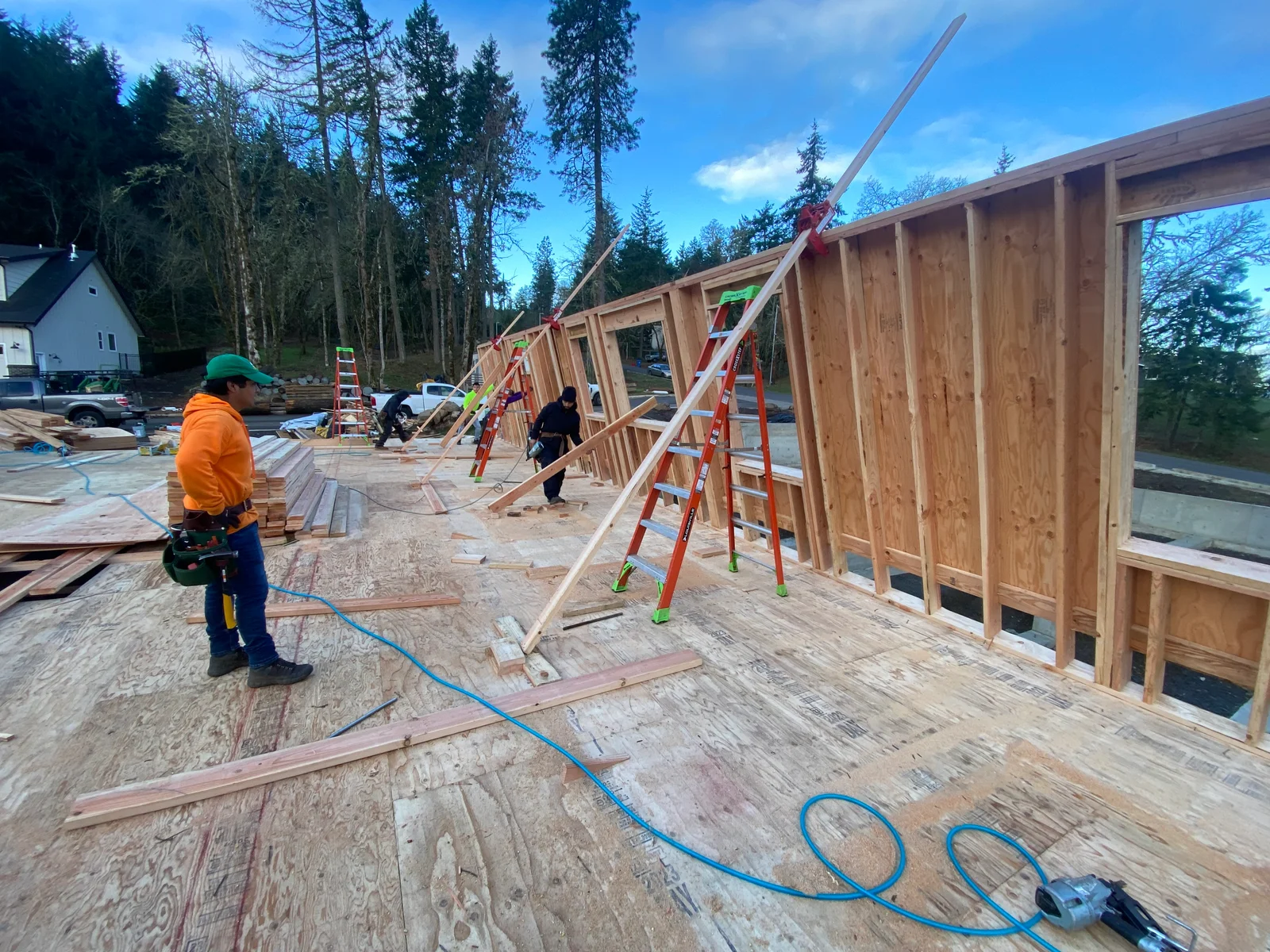 Wood framing and vertical siding installation on residential addition with workers and ladders