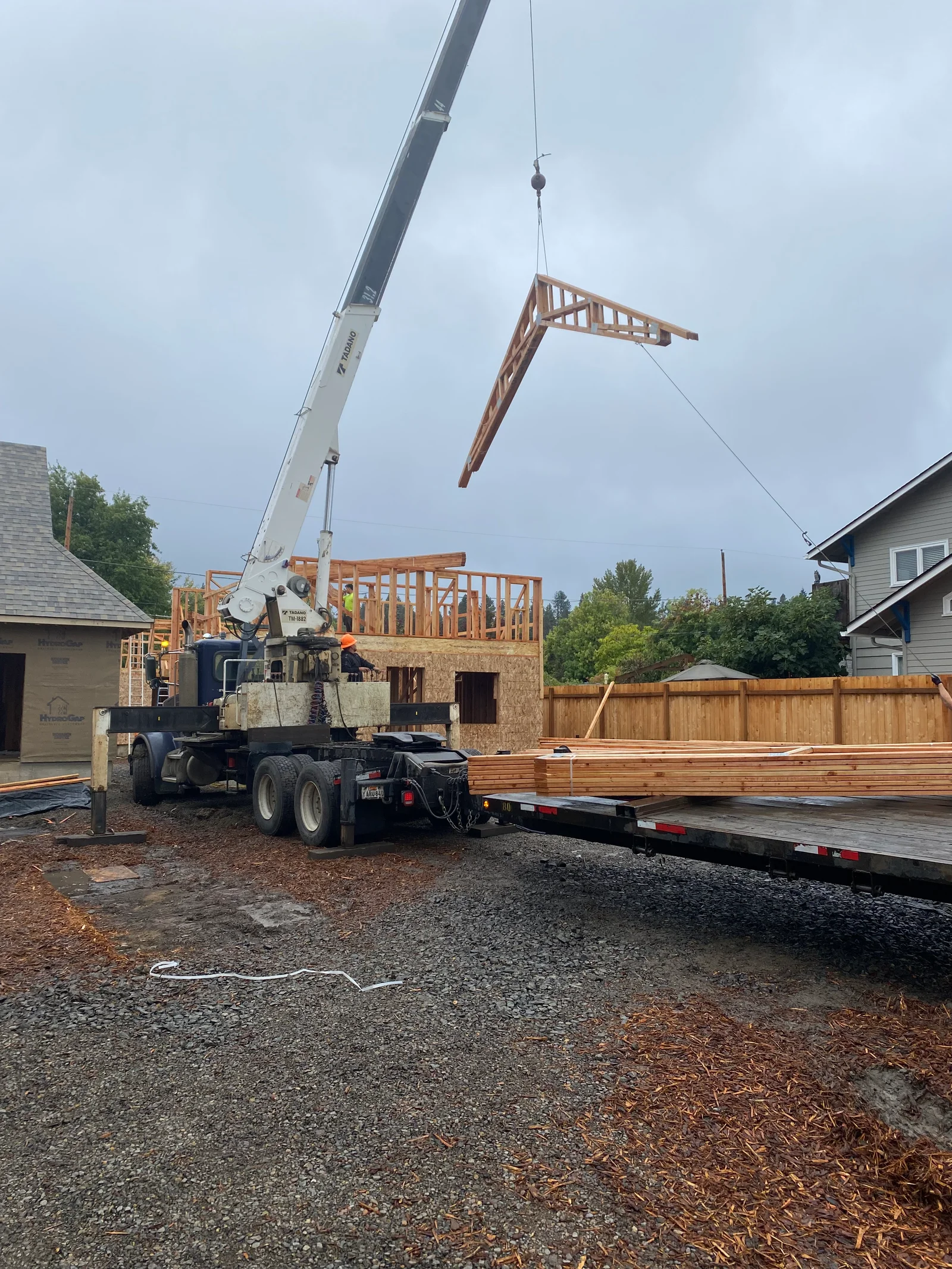 Mobile crane lifting engineered roof truss over residential framing with OSB sheathing and wood structural members