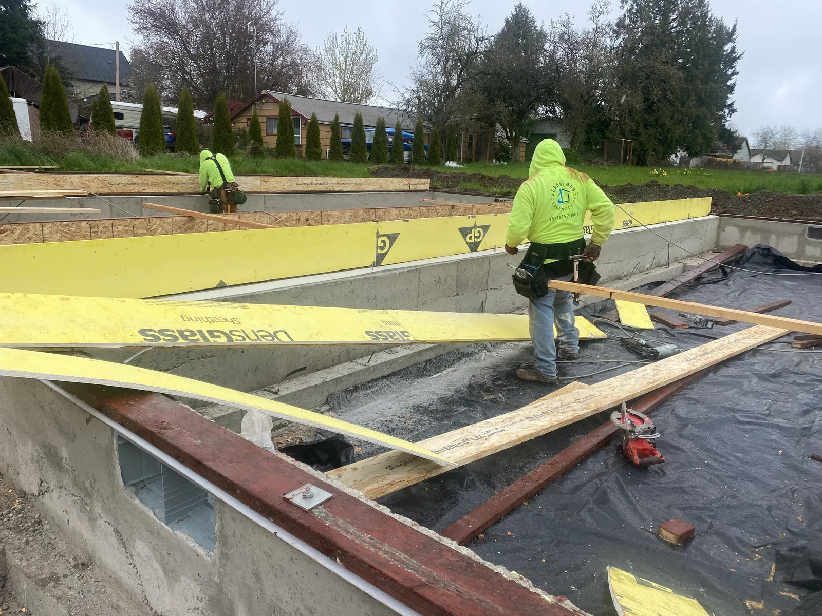 Concrete foundation with black moisture barrier, wooden framing, and yellow safety barriers during installation