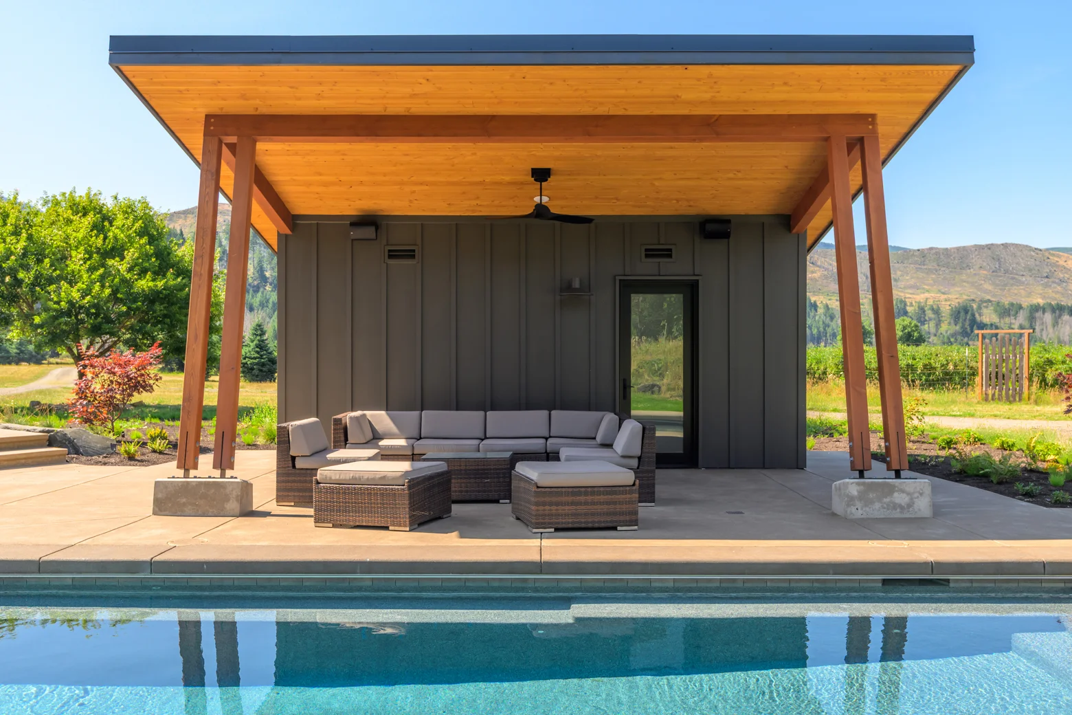 Charcoal vertical siding pool house with cedar soffit, glass door, and steel roof cap
